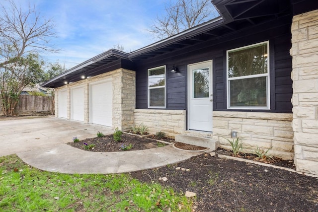 doorway to property with fence, a garage, driveway, and stone siding