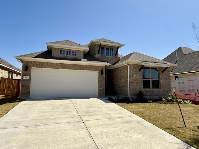 prairie-style house with driveway, brick siding, fence, and a front yard