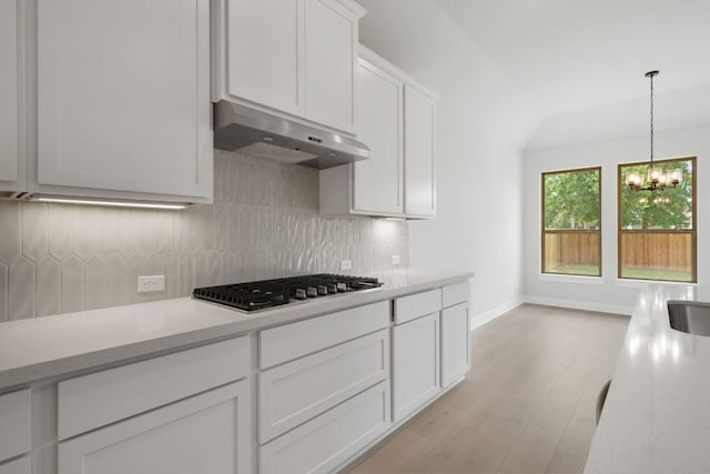 314 Five Mile Creek Way, Kyle, TX 78640 - kitchen featuring under cabinet range hood, stainless steel gas stovetop, a chandelier, tasteful backsplash, and light wood-style floors