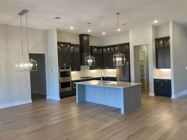 kitchen featuring hanging light fixtures, sink, wall chimney exhaust hood, a large island with sink, and stainless steel appliances