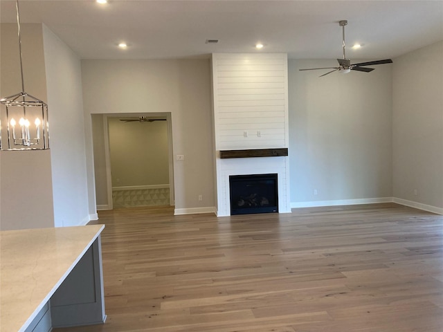 unfurnished living room with light hardwood / wood-style floors, ceiling fan with notable chandelier, and a large fireplace