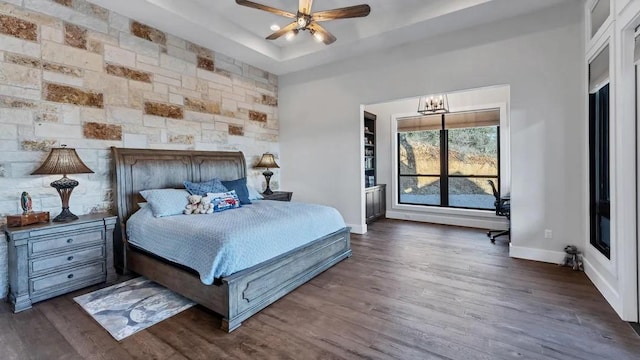 bedroom featuring a raised ceiling, dark hardwood / wood-style flooring, and ceiling fan with notable chandelier