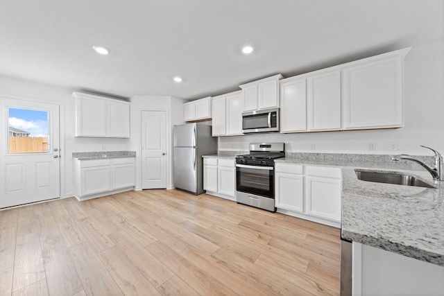 kitchen with white cabinets, appliances with stainless steel finishes, sink, light wood-type flooring, and light stone counters