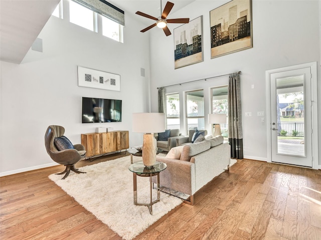 living room featuring ceiling fan, light wood-type flooring, and a high ceiling