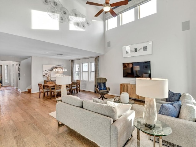 living room featuring baseboards, a high ceiling, ceiling fan, and light wood-style flooring
