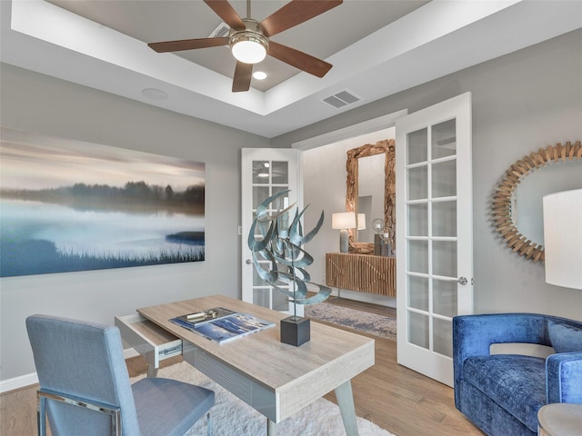 office space with ceiling fan, light hardwood / wood-style flooring, a raised ceiling, and french doors