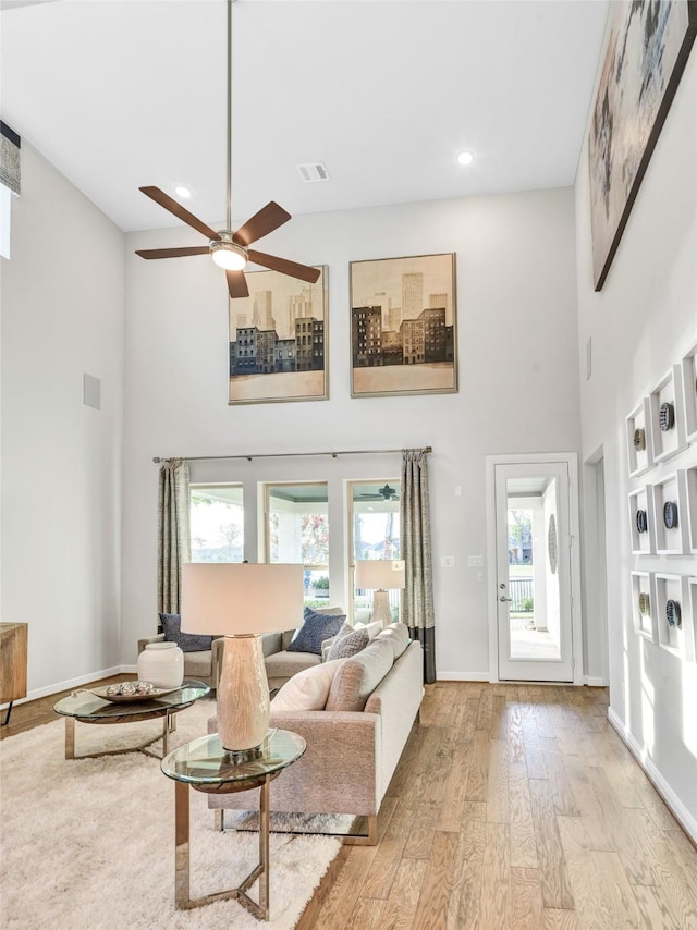 living room with ceiling fan, light hardwood / wood-style floors, and a towering ceiling