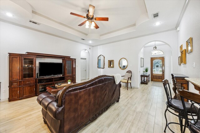 living room with a tray ceiling, light hardwood / wood-style flooring, ornamental molding, and ceiling fan