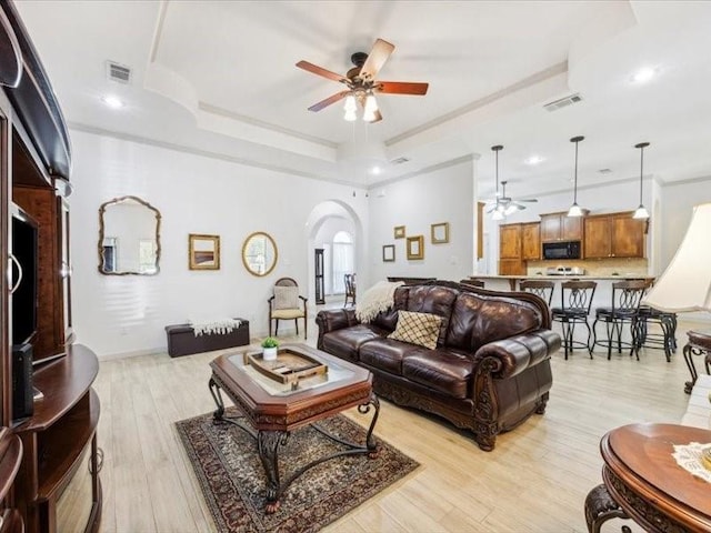 living room featuring a tray ceiling, ceiling fan, and light hardwood / wood-style flooring