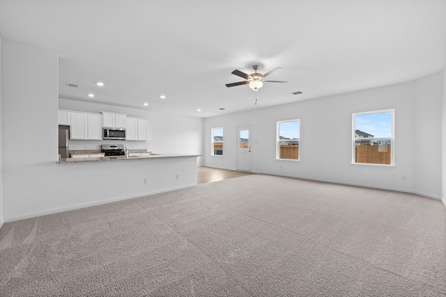 unfurnished living room with ceiling fan, light colored carpet, and sink