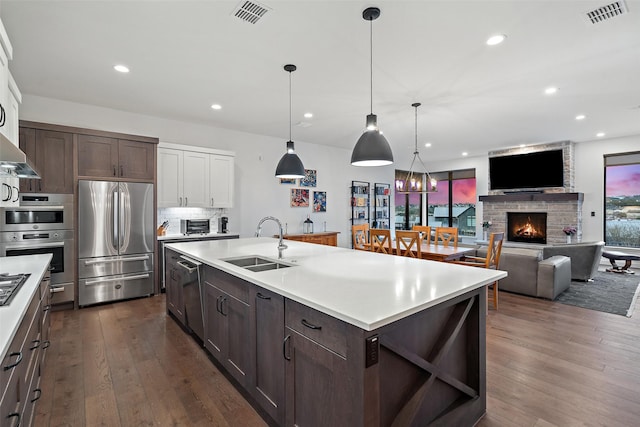 kitchen with decorative light fixtures, stainless steel appliances, sink, a center island with sink, and dark brown cabinets