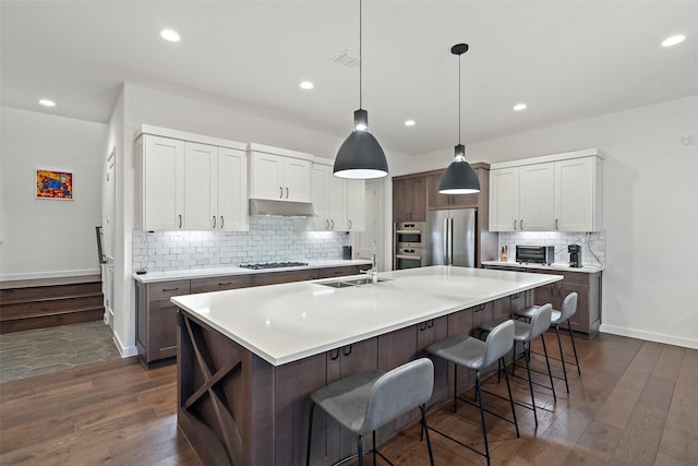 kitchen featuring sink, a kitchen island with sink, a kitchen breakfast bar, stainless steel appliances, and dark hardwood / wood-style flooring