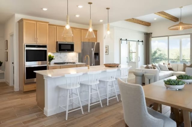 kitchen with stainless steel appliances, beam ceiling, a barn door, and pendant lighting