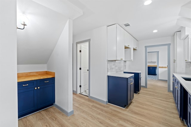 kitchen featuring blue cabinetry, white cabinetry, decorative backsplash, and light wood-type flooring