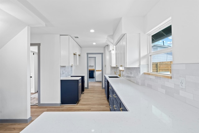 kitchen with white cabinetry, light hardwood / wood-style floors, sink, backsplash, and blue cabinets