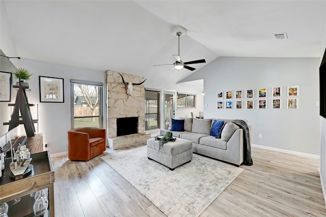 living room featuring light hardwood / wood-style floors, ceiling fan, a stone fireplace, and vaulted ceiling