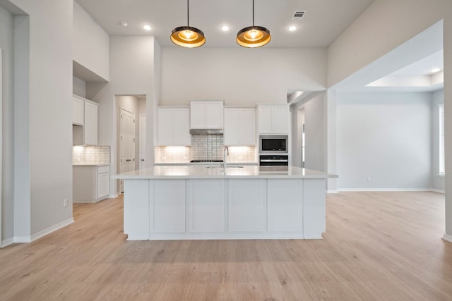 305 Five Mile Creek Way, Kyle, TX 78640 - kitchen with decorative backsplash, light countertops, white cabinetry, light wood finished floors, and built in microwave