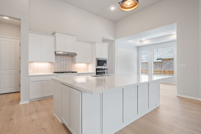 305 Five Mile Creek Way, Kyle, TX 78640 - kitchen with light wood-type flooring, an island with sink, backsplash, built in microwave, and white cabinets