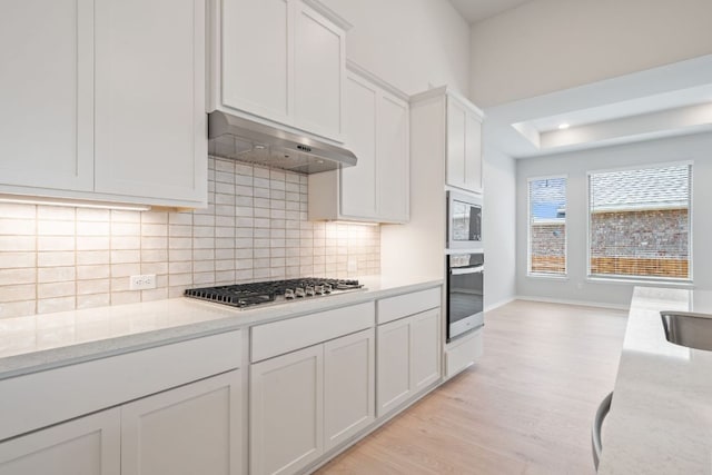 305 Five Mile Creek Way, Kyle, TX 78640 - kitchen featuring stainless steel appliances, ventilation hood, backsplash, light wood finished floors, and light stone countertops