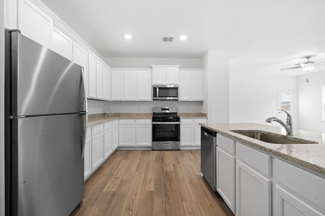 kitchen with light stone countertops, white cabinets, stainless steel appliances, light hardwood / wood-style floors, and sink