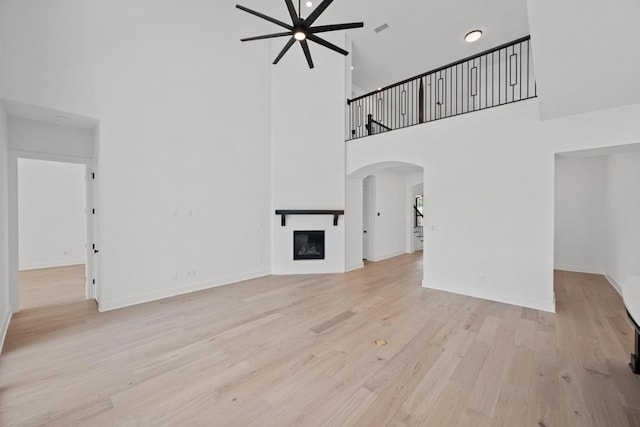 162 Leaning Rock Rdg, Austin, TX 78737 - unfurnished living room with a towering ceiling, a ceiling fan, arched walkways, wood finished floors, and a fireplace