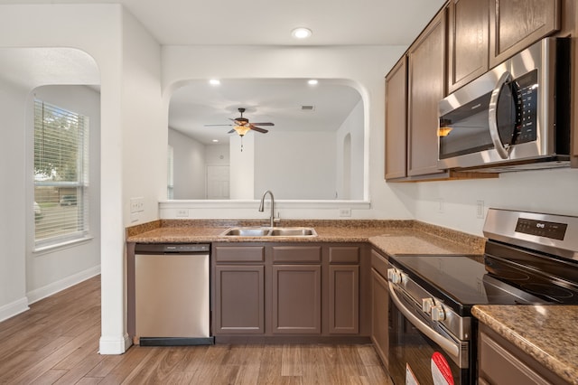 kitchen with stainless steel appliances, dark stone counters, light hardwood / wood-style floors, sink, and ceiling fan