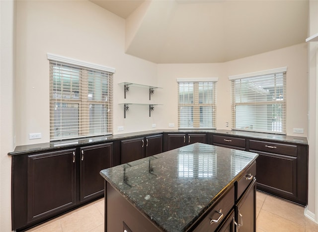 kitchen with light tile patterned floors, a center island, dark brown cabinets, and dark stone counters