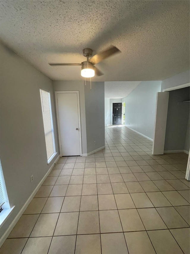 empty room featuring ceiling fan, light tile patterned flooring, and a textured ceiling