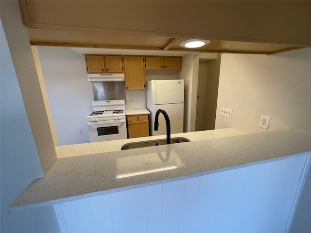 kitchen with light stone counters, sink, white appliances, and kitchen peninsula