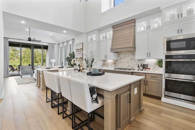 kitchen featuring a spacious island, white cabinets, appliances with stainless steel finishes, decorative backsplash, and a kitchen breakfast bar