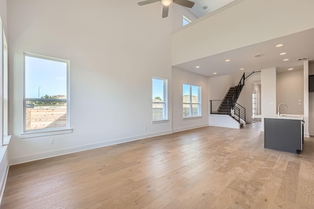 unfurnished living room with sink, light wood-type flooring, a towering ceiling, and ceiling fan