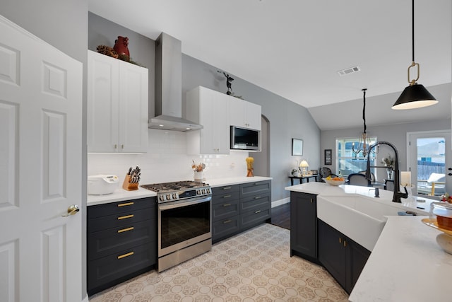 kitchen featuring white cabinetry, stainless steel range with gas cooktop, hanging light fixtures, wall chimney range hood, and sink