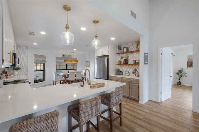 kitchen with a kitchen bar, backsplash, hanging light fixtures, stainless steel fridge, and kitchen peninsula