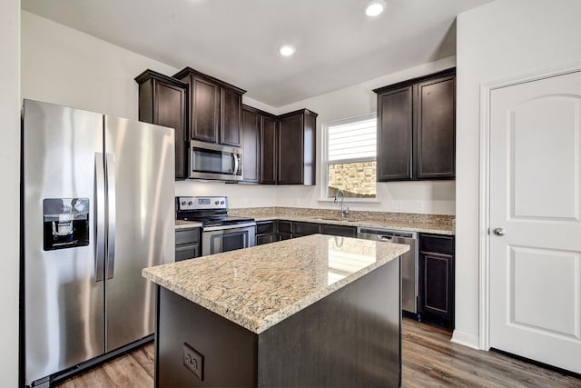 kitchen featuring hardwood / wood-style flooring, stainless steel appliances, light stone countertops, a kitchen island, and dark brown cabinetry