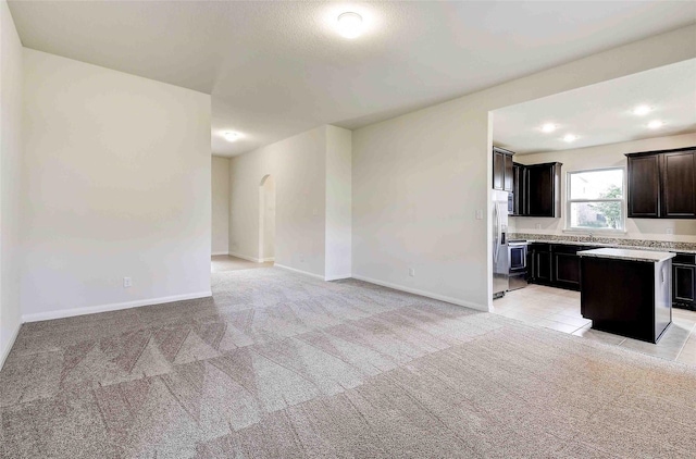 kitchen with light carpet, a kitchen island, dark brown cabinets, and stainless steel fridge