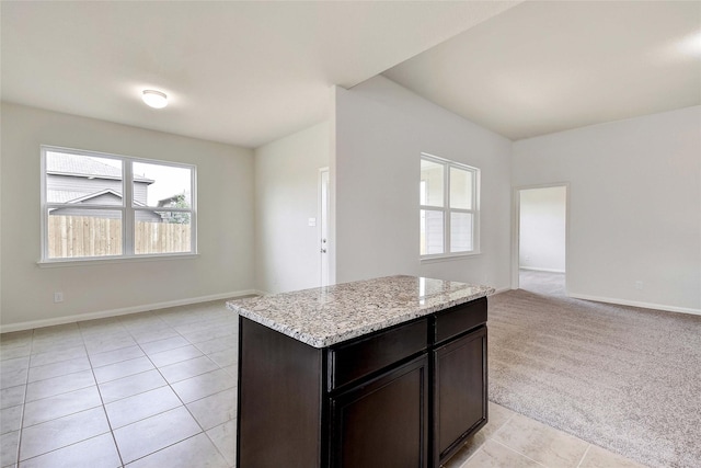 kitchen with light carpet, dark brown cabinets, light stone counters, and a center island