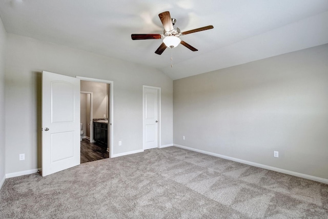 unfurnished bedroom with ceiling fan, ensuite bath, vaulted ceiling, and dark carpet