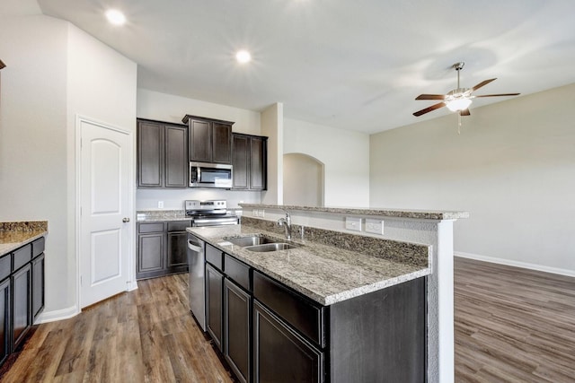 kitchen with dark brown cabinetry, dark hardwood / wood-style flooring, stainless steel appliances, sink, and a center island with sink