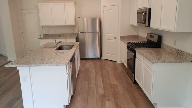 kitchen featuring light stone countertops, white cabinets, appliances with stainless steel finishes, sink, and a center island with sink