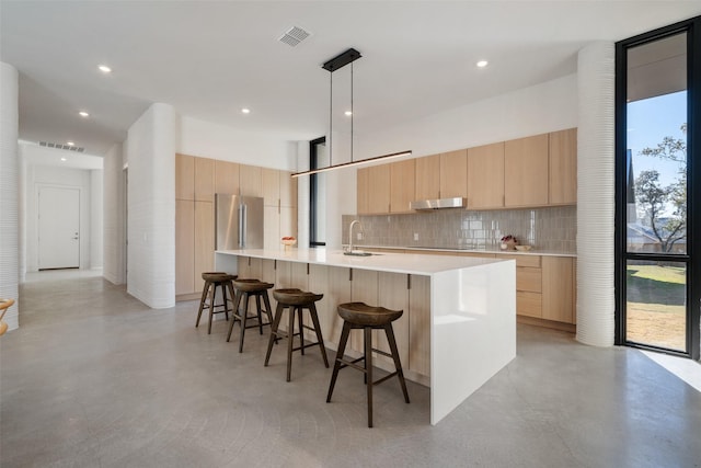 kitchen featuring light brown cabinets, a healthy amount of sunlight, sink, hanging light fixtures, and a breakfast bar area