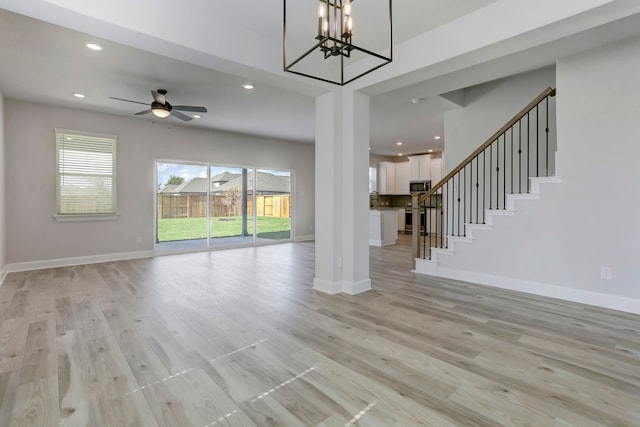 unfurnished living room with light wood-type flooring and ceiling fan with notable chandelier