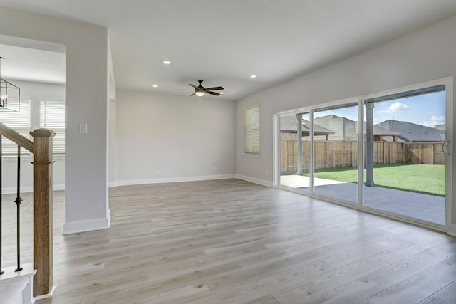 unfurnished living room with ceiling fan with notable chandelier and light hardwood / wood-style flooring