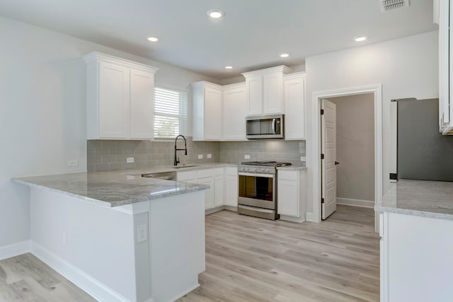 kitchen with white cabinetry, stainless steel appliances, tasteful backsplash, kitchen peninsula, and light hardwood / wood-style flooring