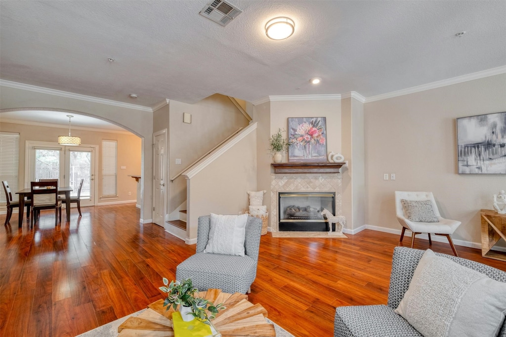 living room with hardwood / wood-style flooring, a textured ceiling, a tile fireplace, and crown molding