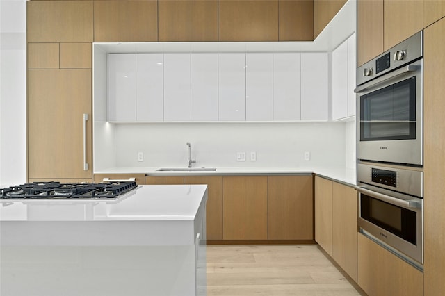 kitchen featuring light wood-type flooring, appliances with stainless steel finishes, sink, and light brown cabinets