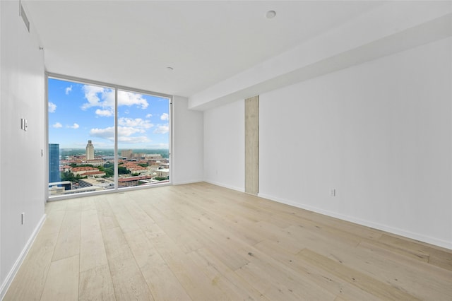 spare room with a wall of windows and light hardwood / wood-style flooring