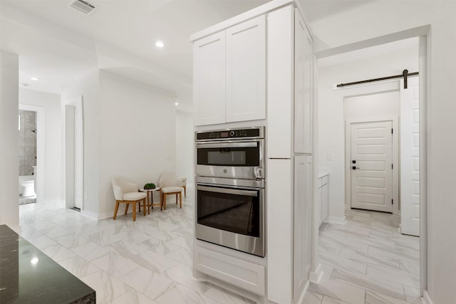 kitchen with double oven, a barn door, white cabinets, and dark stone counters