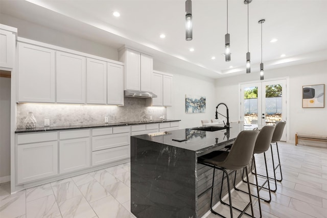 kitchen with pendant lighting, white cabinetry, french doors, sink, and a kitchen island with sink