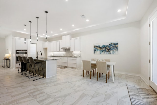 kitchen featuring pendant lighting, white cabinets, tasteful backsplash, and a kitchen island with sink