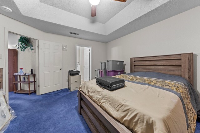 carpeted bedroom featuring a textured ceiling, ceiling fan, and a raised ceiling